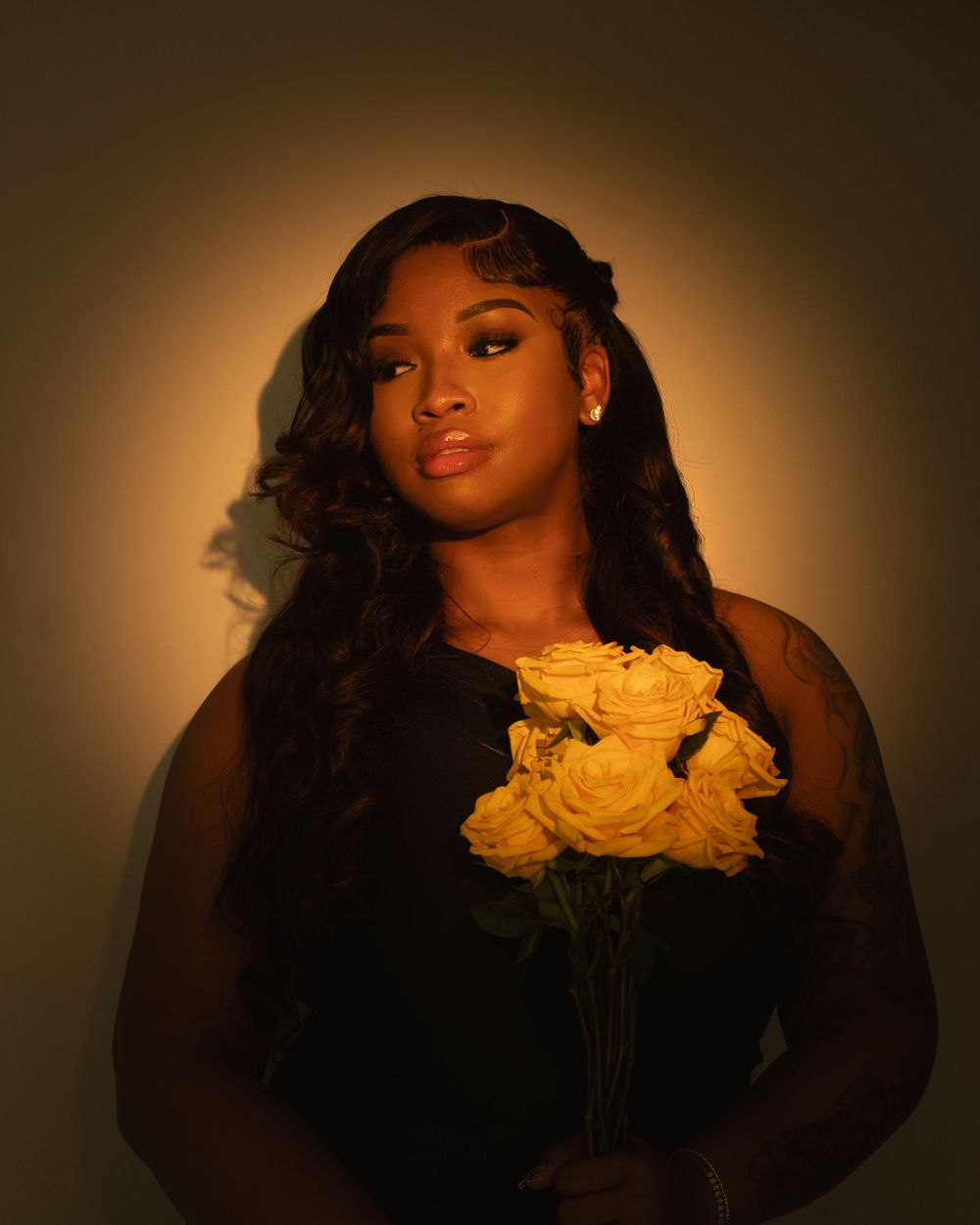 Moody portrait with someone holding yellow roses against warm lighting.