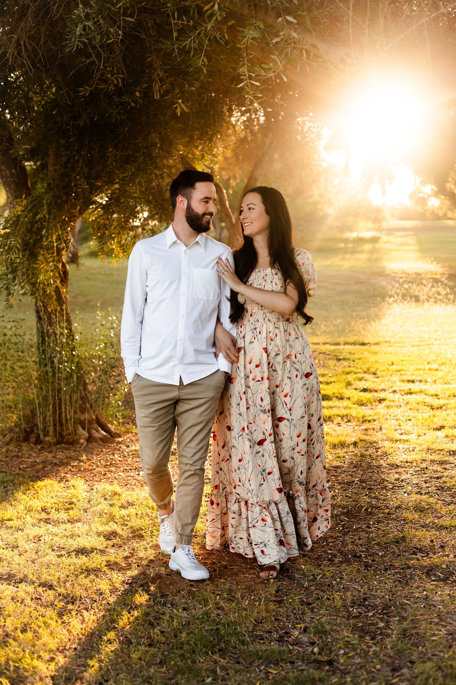 A walking couple staring in each others eyes during their engagement portrait session with the golden glow shining through the olive trees.