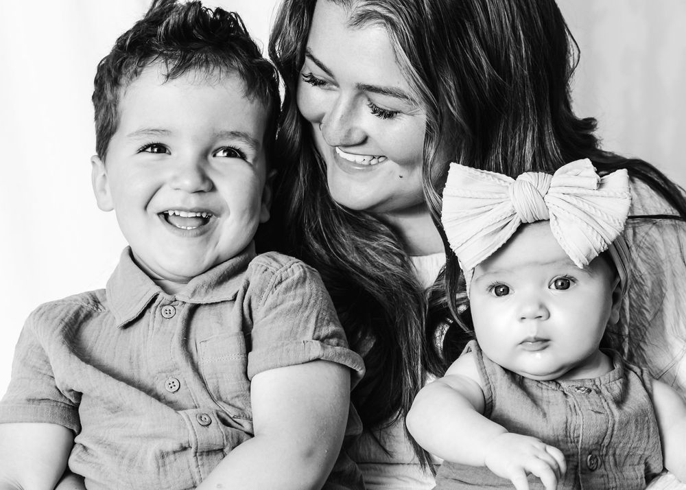 Black and white portrait of a mother with her two young children sharing joyful expressions together.