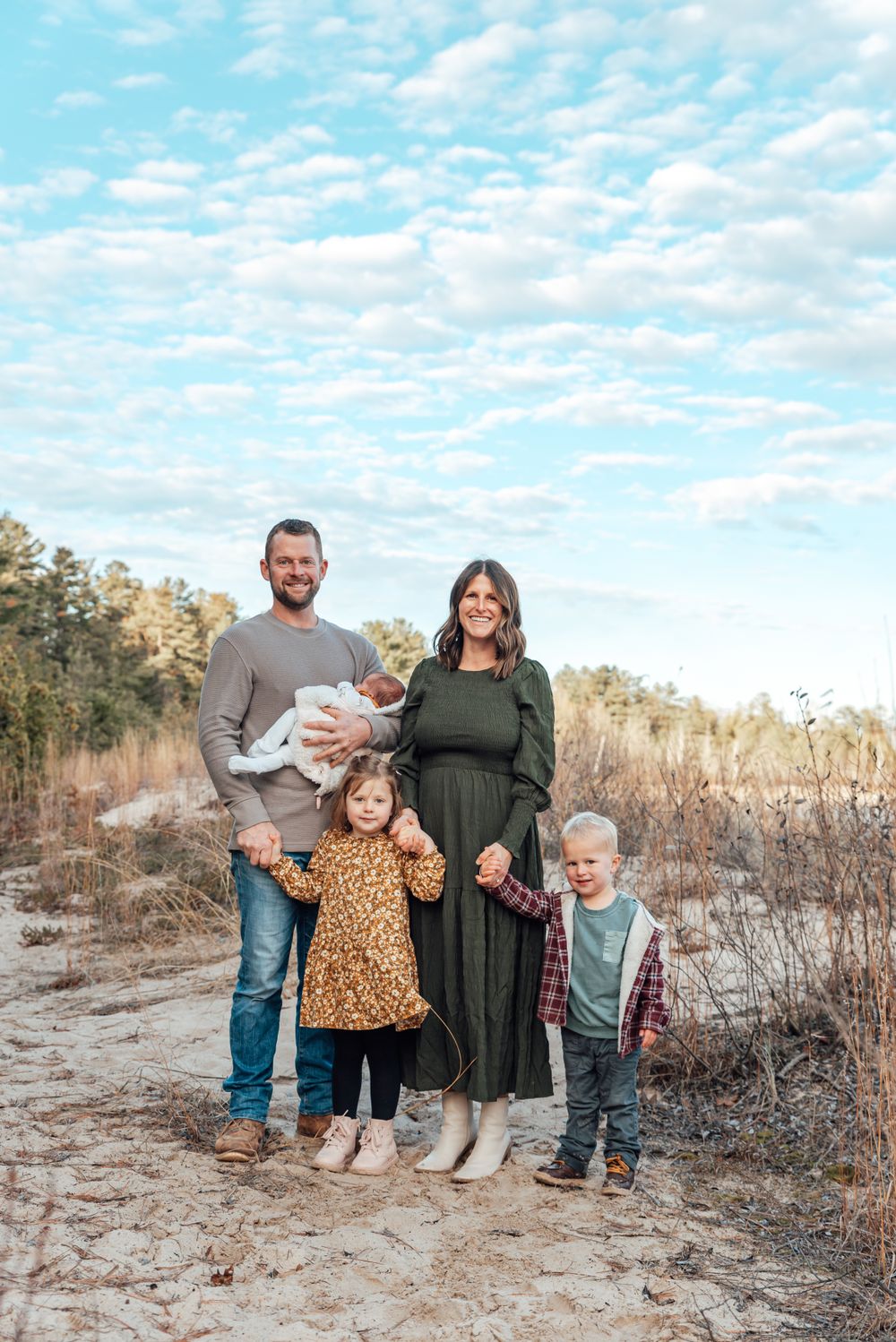 Family of five posing outdoors against cloudy sky in winter landscape.