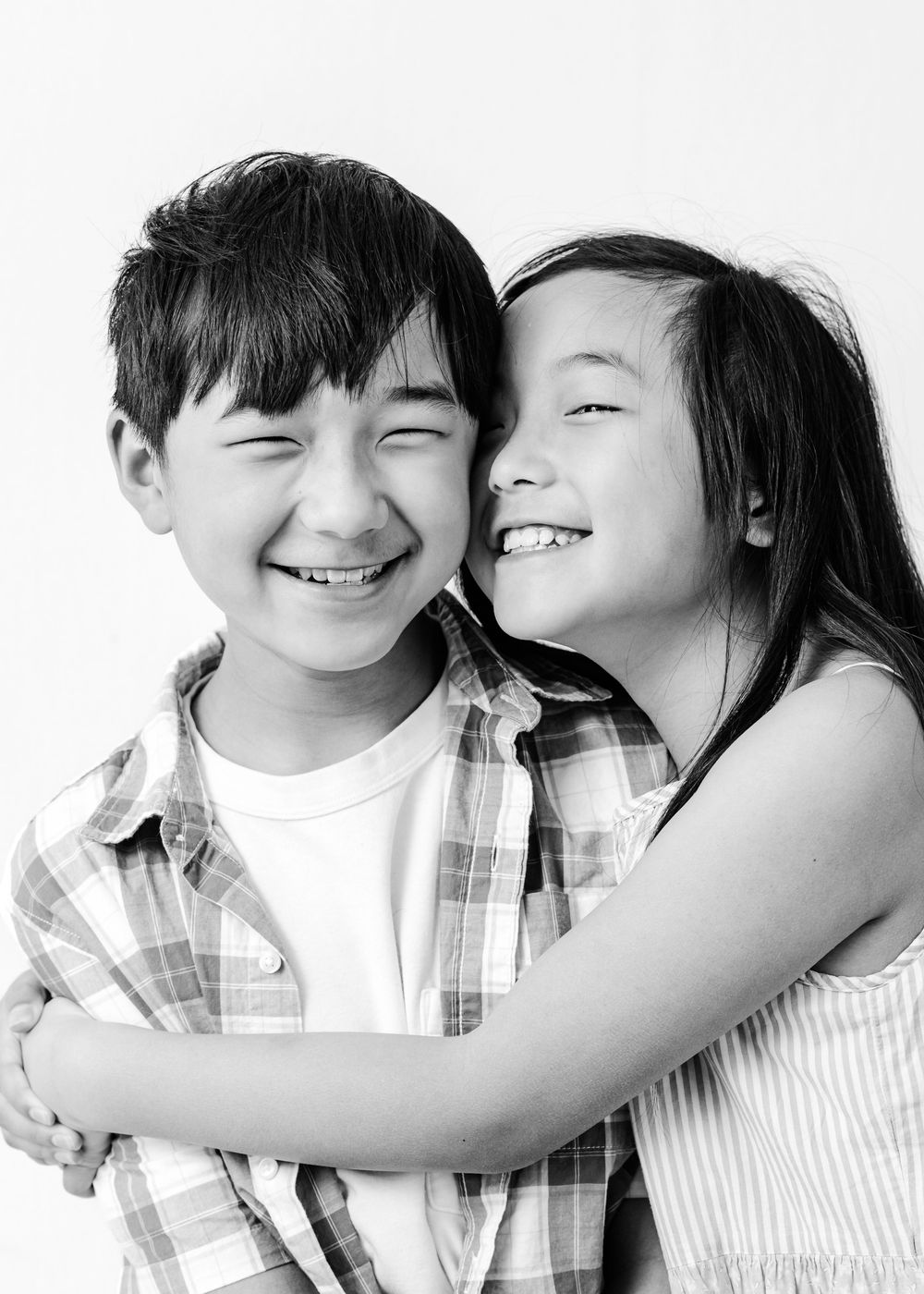 Two joyful children sharing a tender embrace and genuine smiles in a black and white portrait.