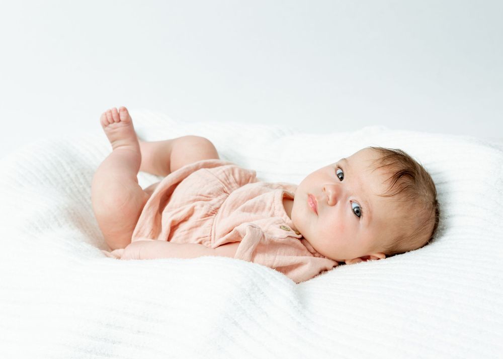 A baby is lying on a white blanket in various poses showing different angles and expressions.
