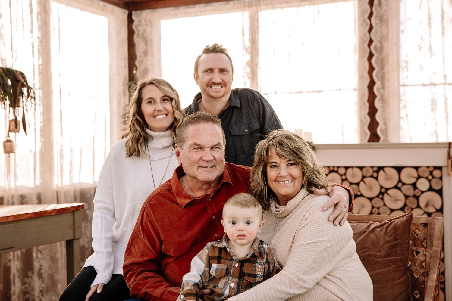 family of 4 posing in a greenhouse huging and laughing enjoying thier time together with baby on grandparents lap. liz rivas colorado photog