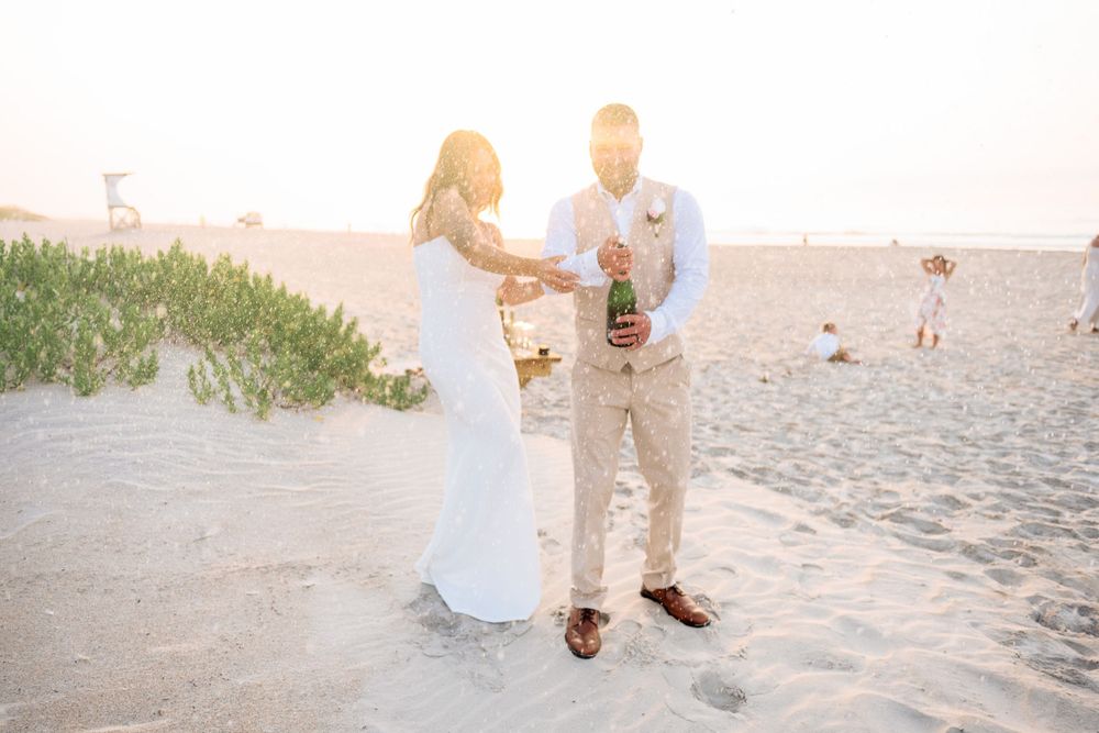 A couple shares a romantic moment at sunset on a beach while holding drinks.