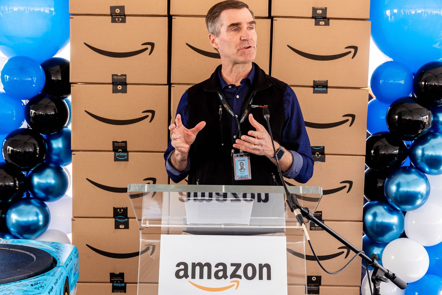 Speaker at an Amazon event podium with branded backdrop and blue and black balloon decorations.