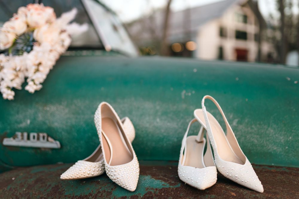 White sparkly bridal shoes displayed on teal vintage surface with floral decorations.