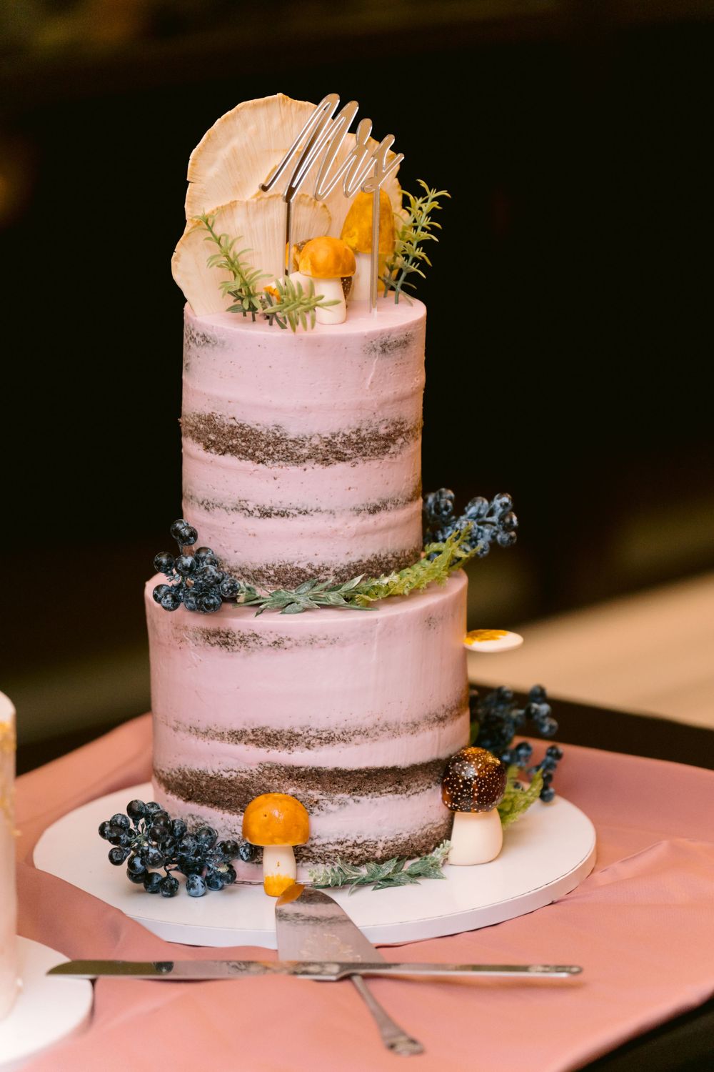 Three-tiered pink wedding cake decorated with blueberries, citrus and metallic accents.