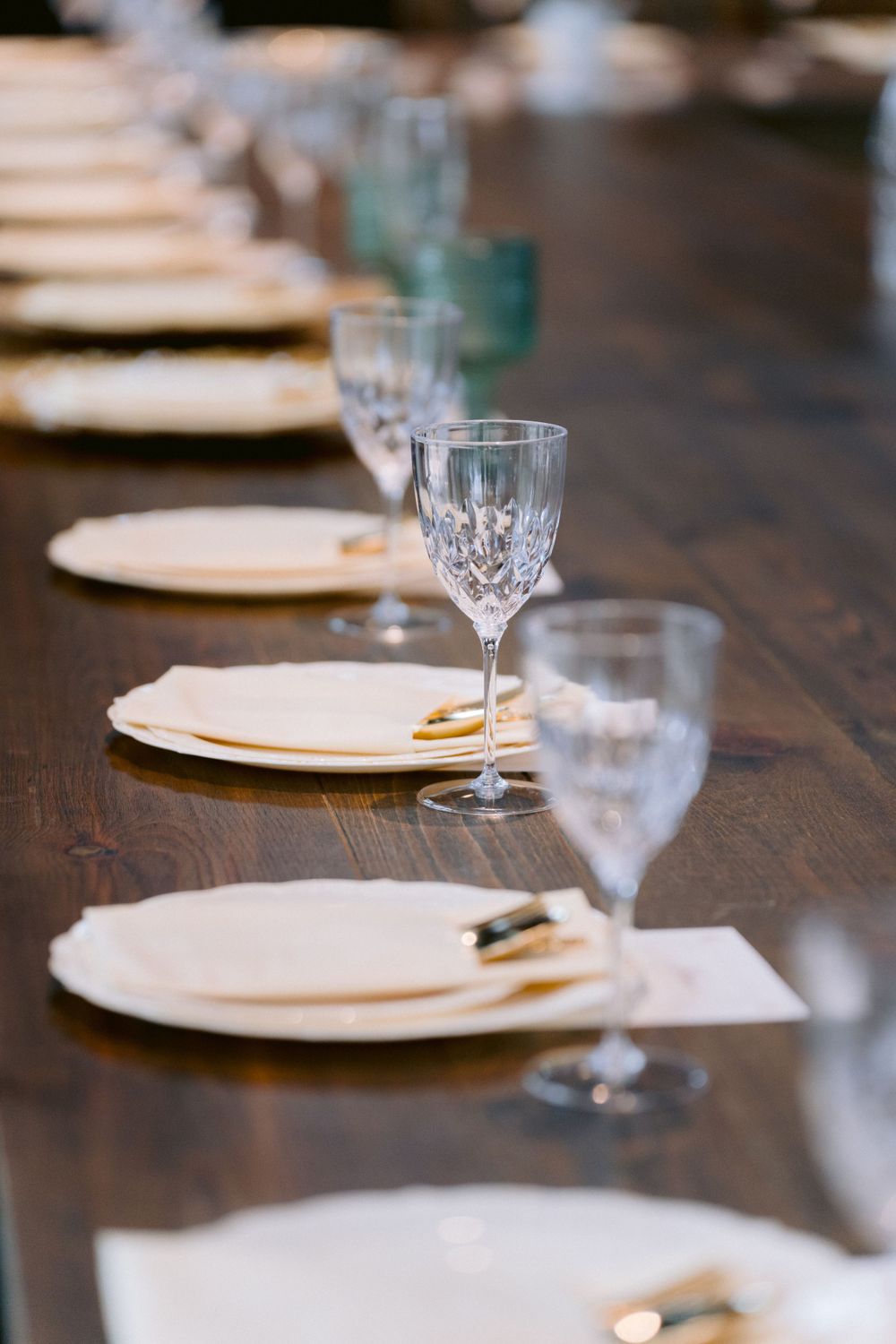 Place settings with crystal wine glasses and white plates arranged on a dark wooden table.
