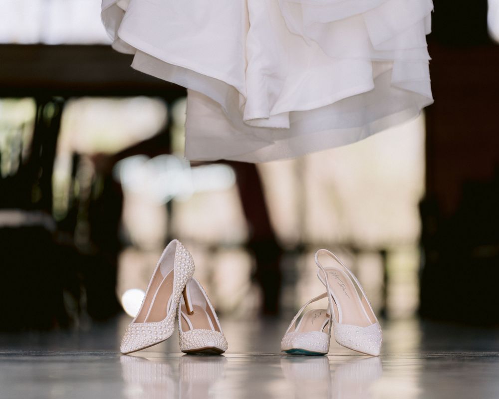 Elegant white bridal heels photographed against a dark floor.