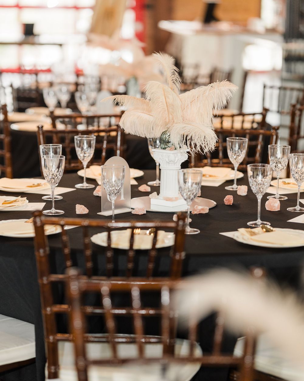 Elegant wedding reception table with black linens, crystal glasses, and white feather centerpieces.