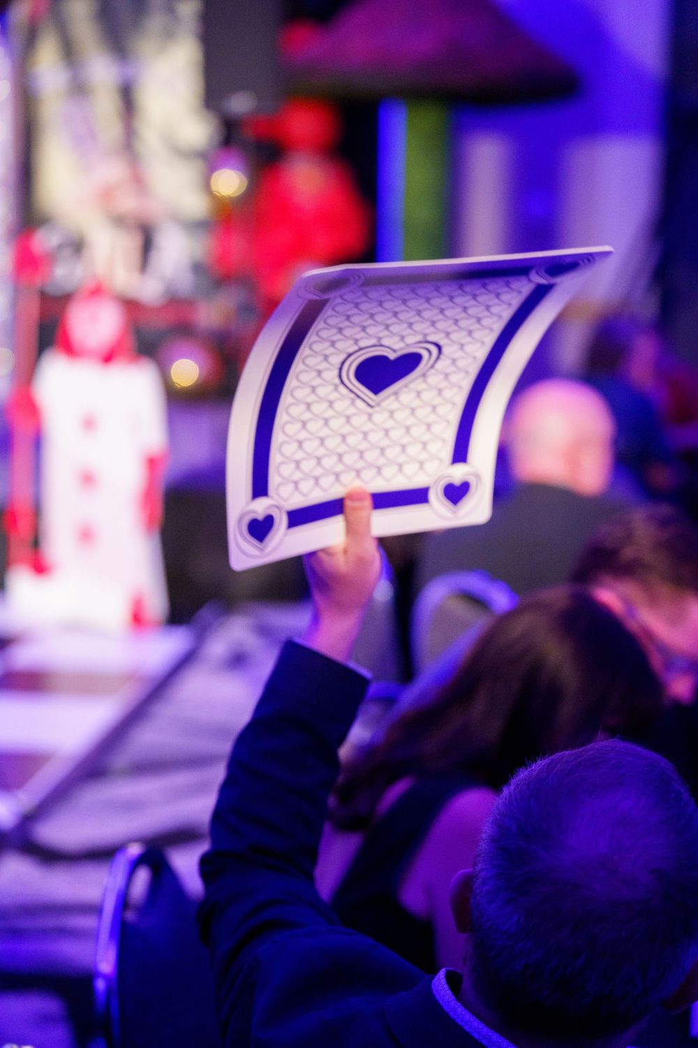 Someone holds up a card with heart designs during a purple-lit event with blurred background lights.