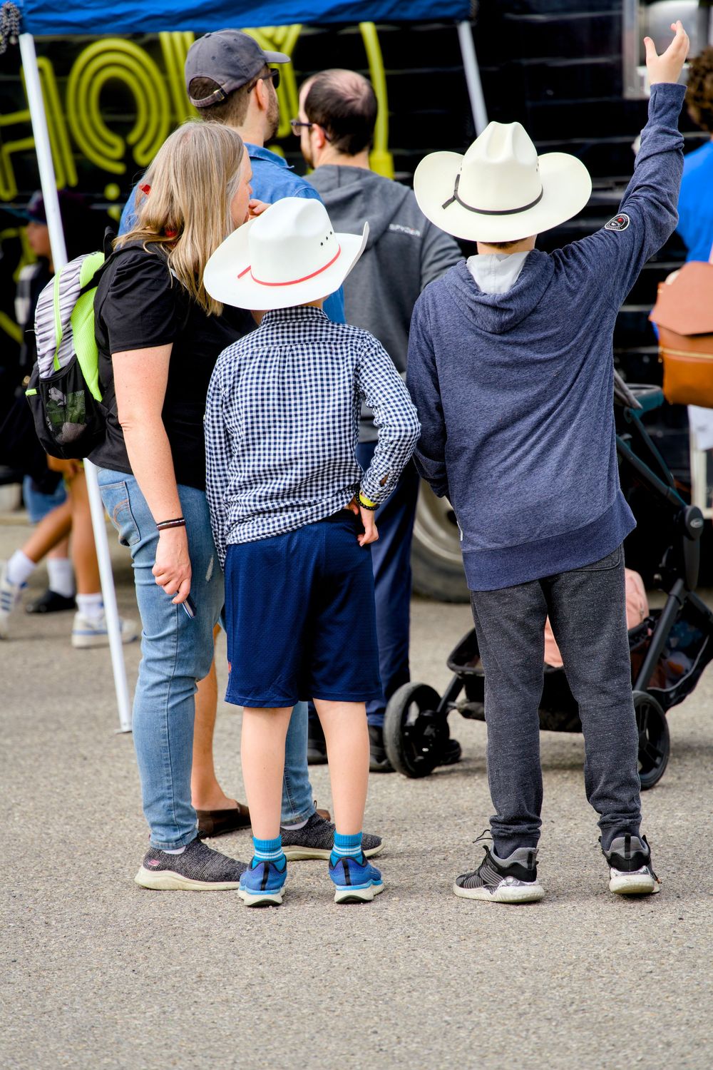 Crowd of people standing together at an outdoor event, shown from waist down with some wearing cowboy hats.