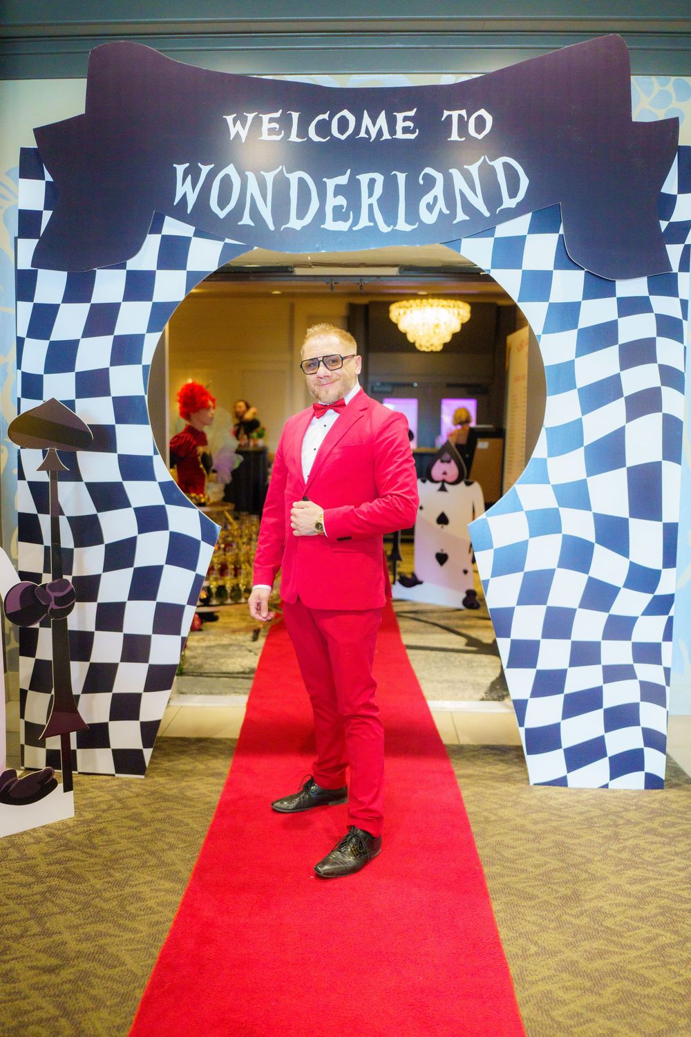 "Welcome to Wonderland" entrance arch with black and white checkered pattern and red carpet at a special event.