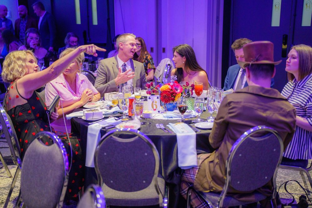 A group of guests enjoying a dinner gathering at a formal event with purple lighting and elegant table settings.