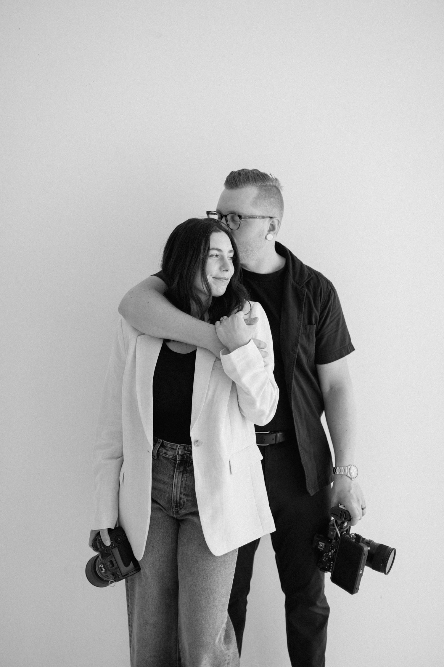 Two photographers in casual attire holding cameras against a grey background.