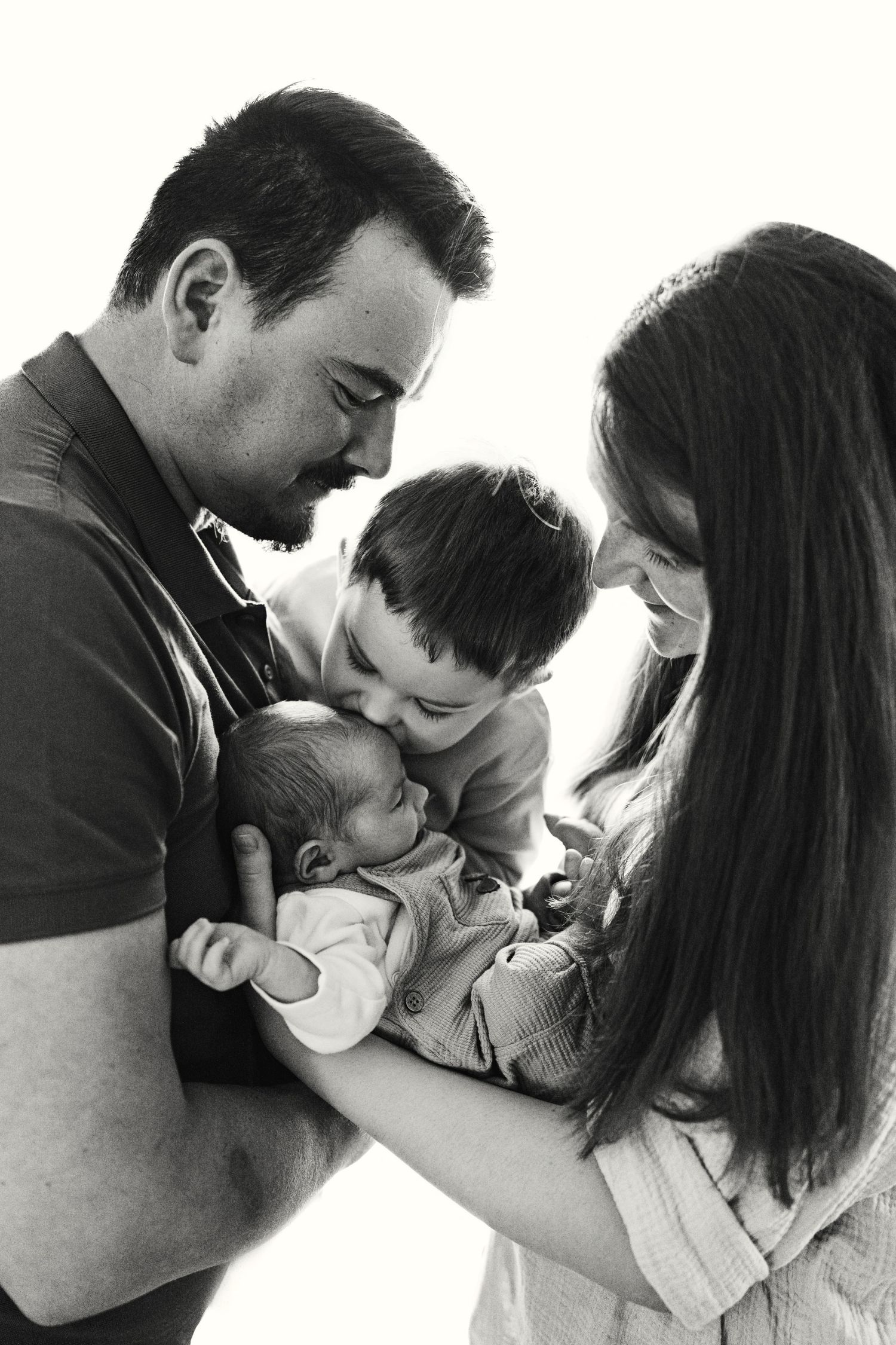 Black and white portrait of a family gathered close together looking adoringly at their newborn baby.