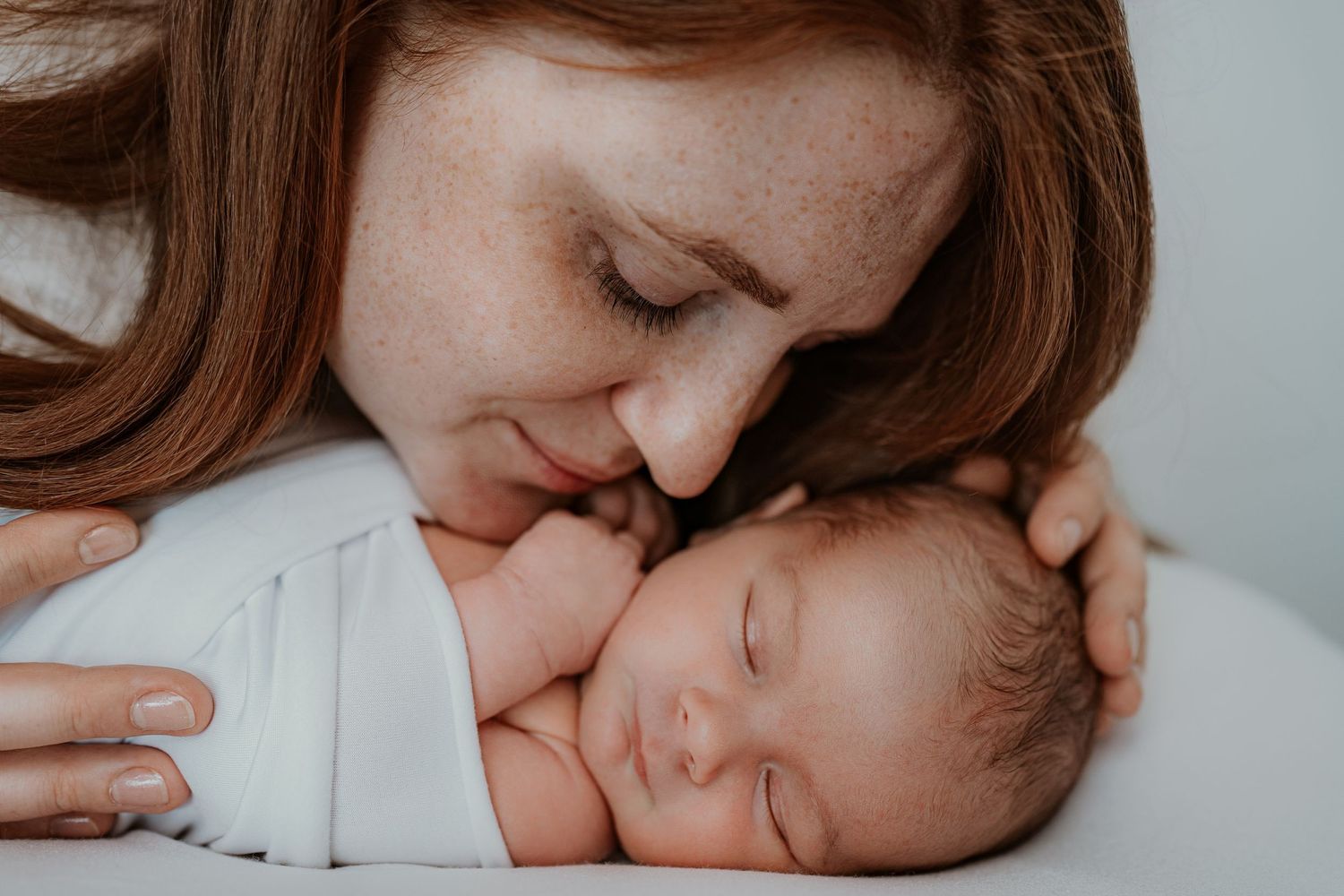 A nurturing parent tenderly cuddles and kisses their sleeping newborn baby in a soft, intimate moment.