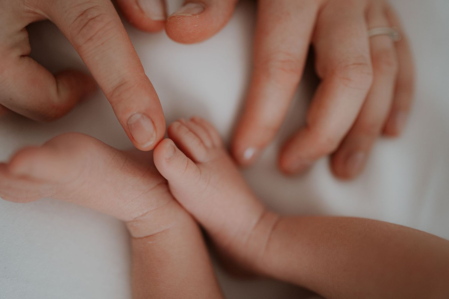 Close-up shot of hands gently holding a baby's tiny fingers against a white background.