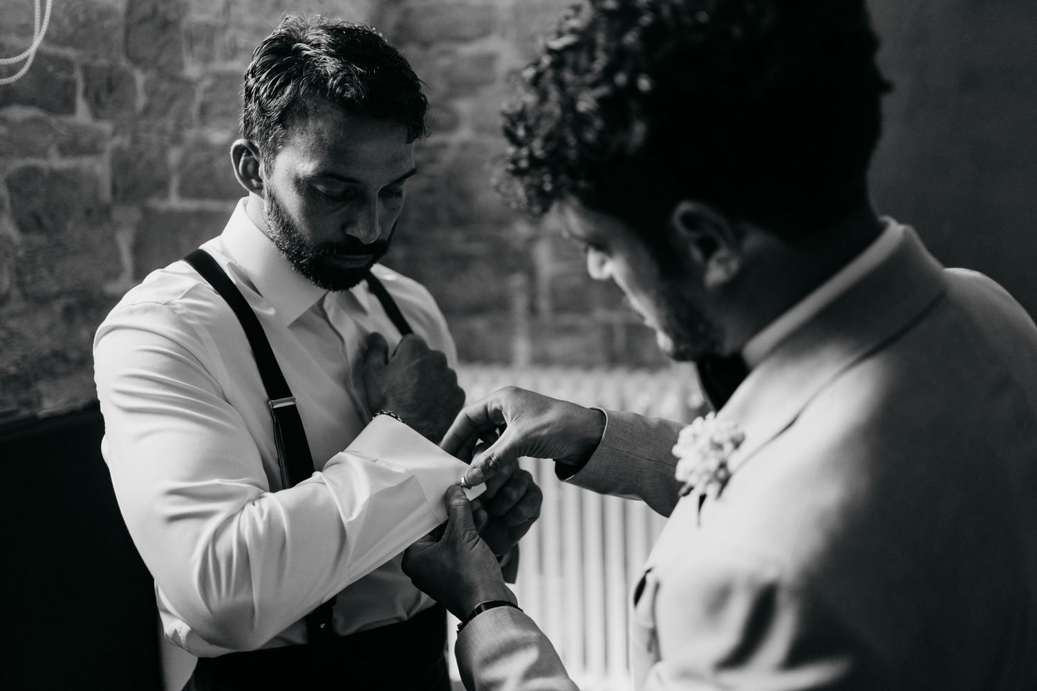 Two people in formal attire helping each other with accessories in black and white.