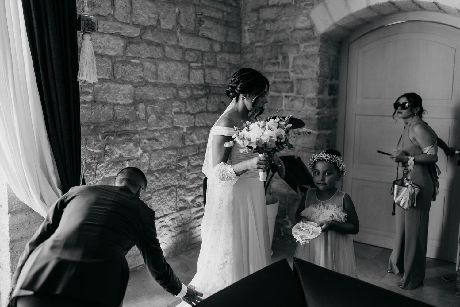 A candid wedding moment captured in black and white against a stone wall backdrop.