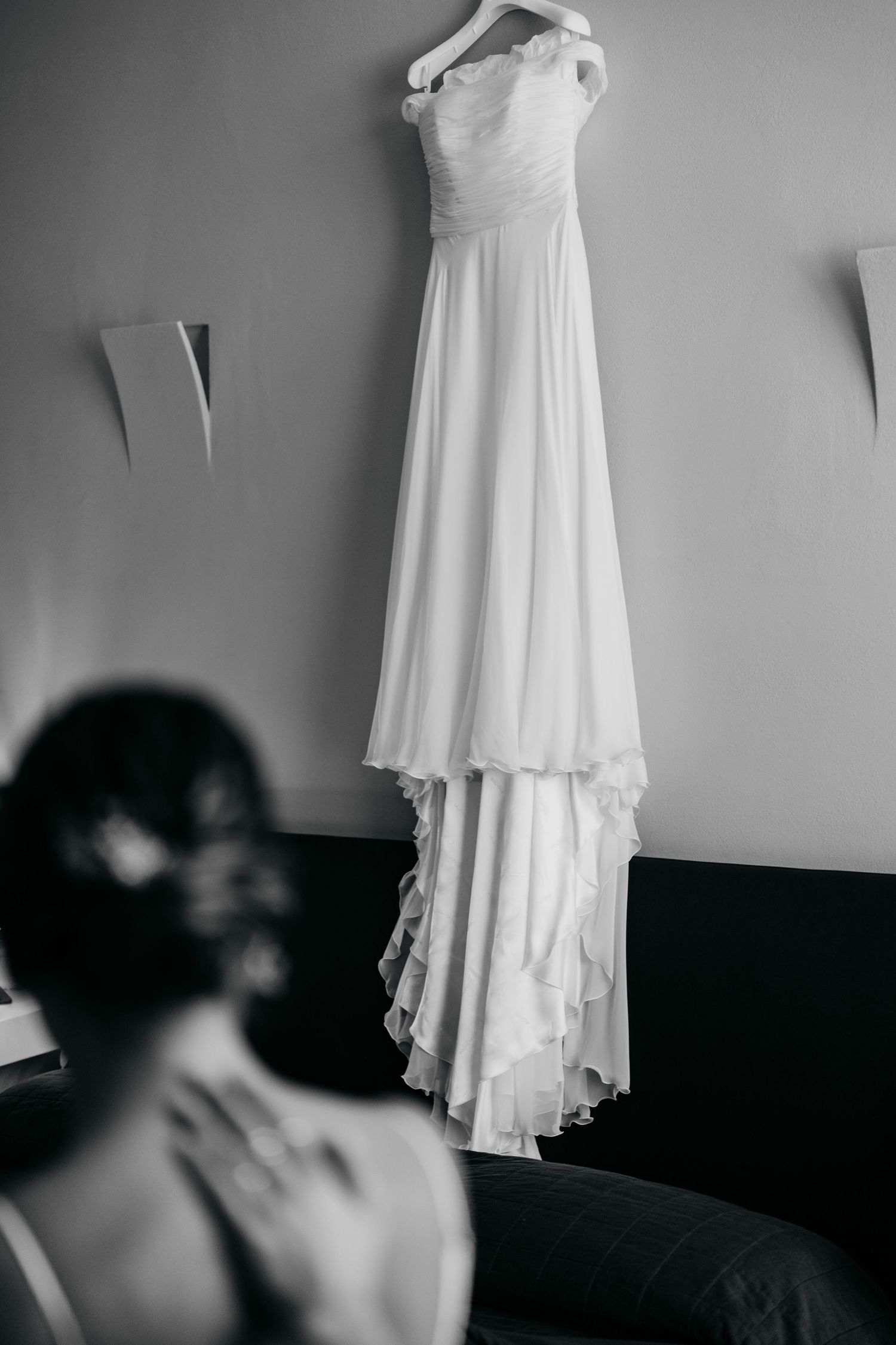 Elegant white wedding dress hangs on display while being viewed in a black and white photo.