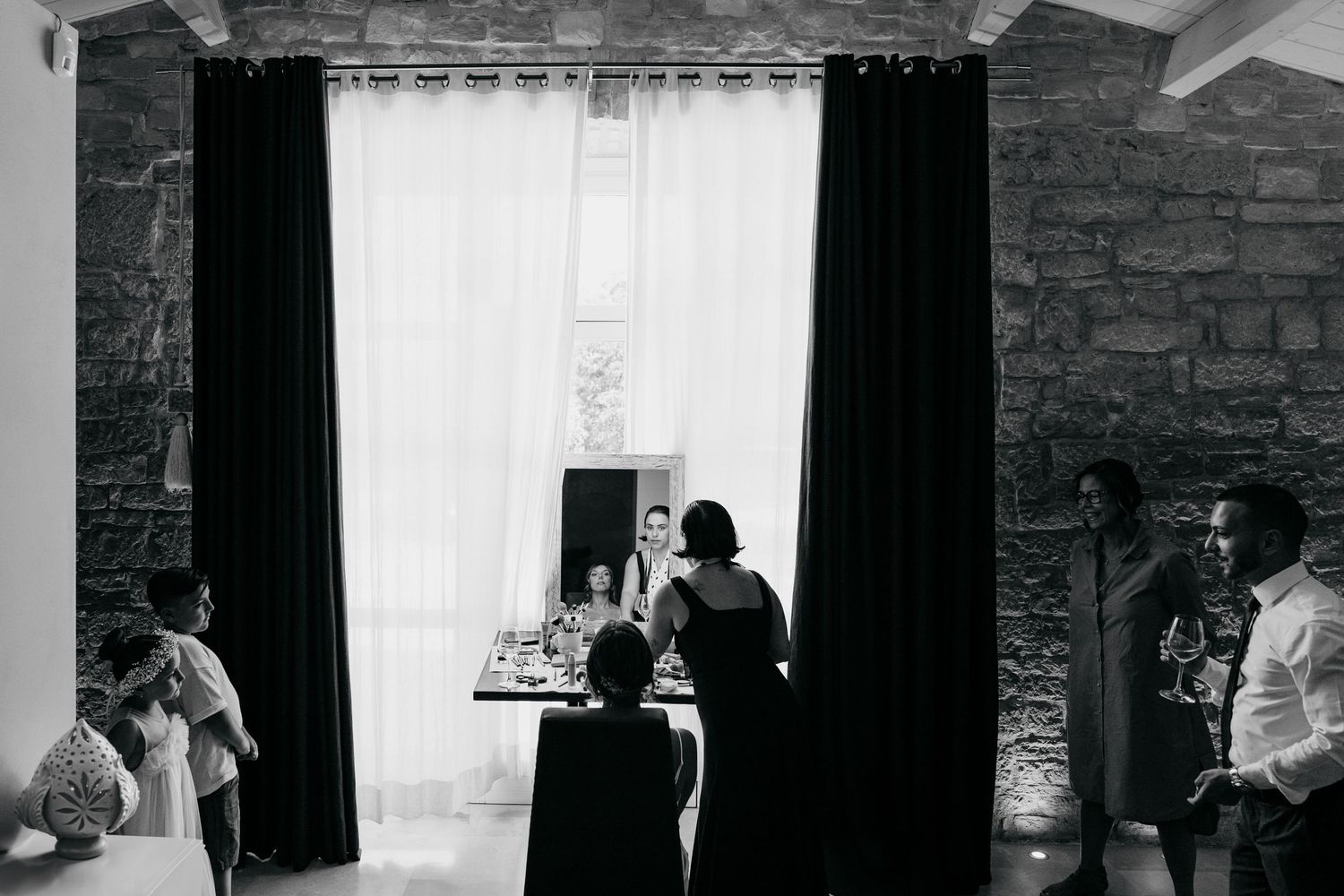 Black and white photo showing wedding preparations in a rustic stone-walled room with curtains.