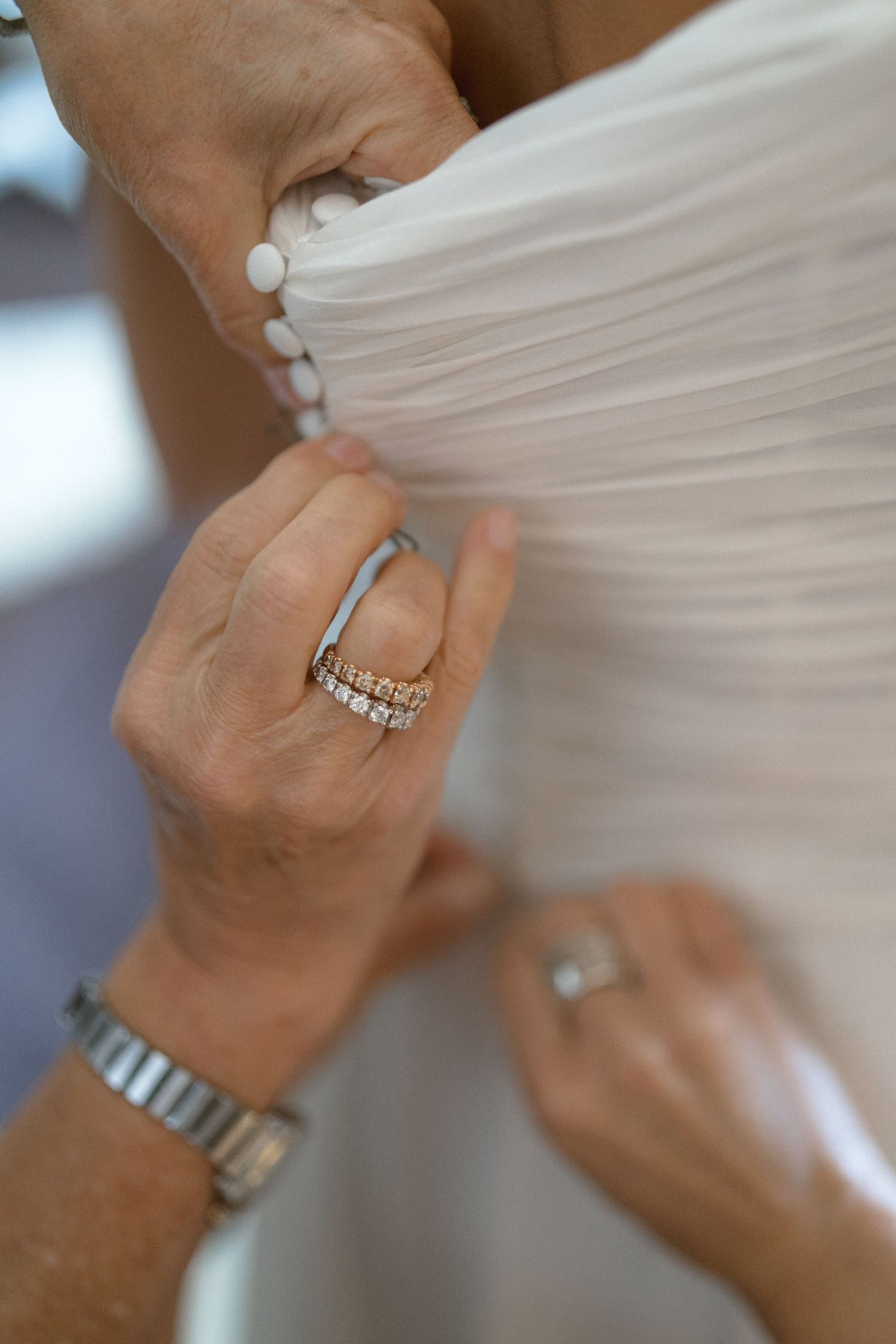 Close-up detail shots of wedding rings and jewelry against white dress fabric.