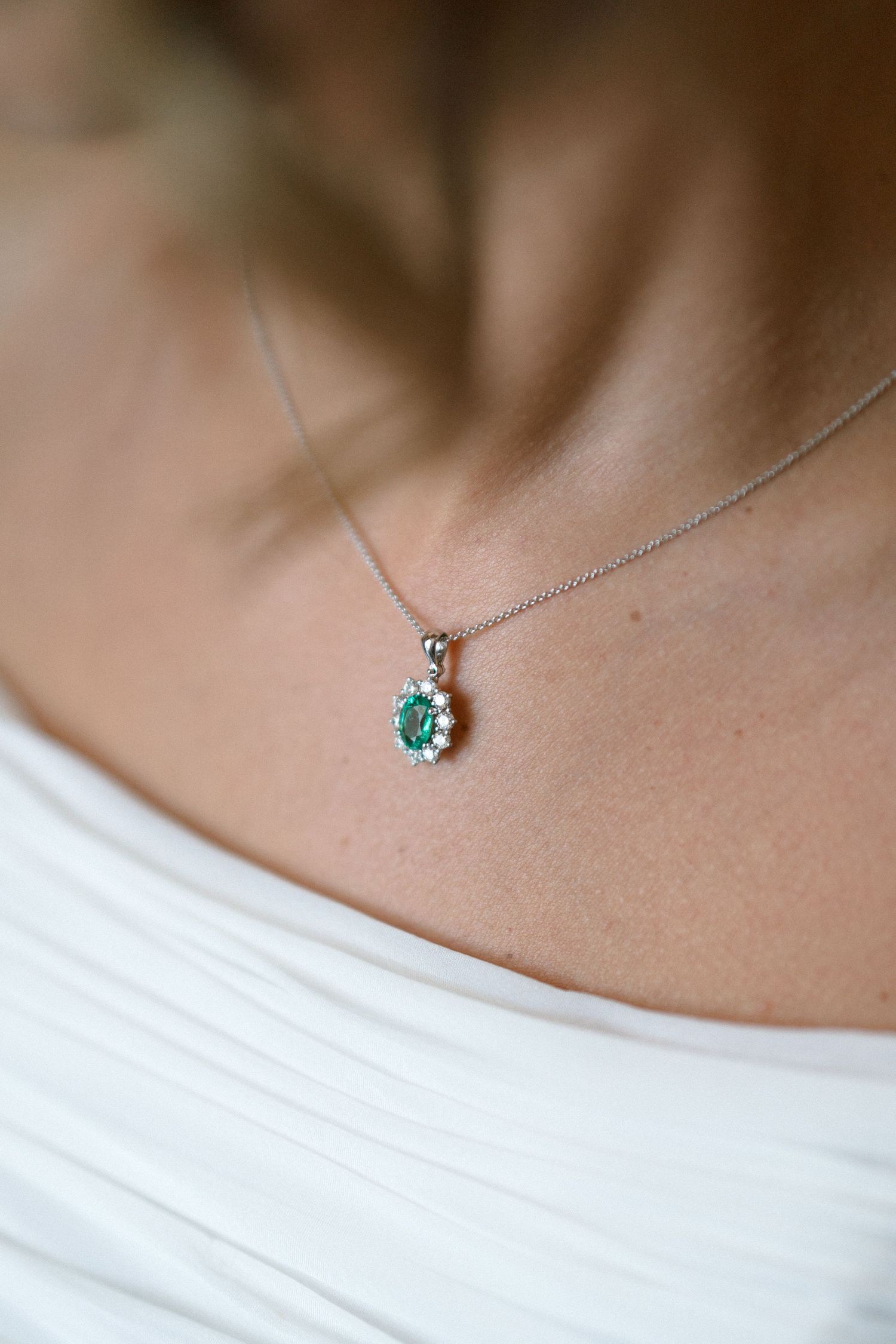 A delicate silver necklace featuring a small teal gemstone pendant rests elegantly against smooth skin and white fabric.