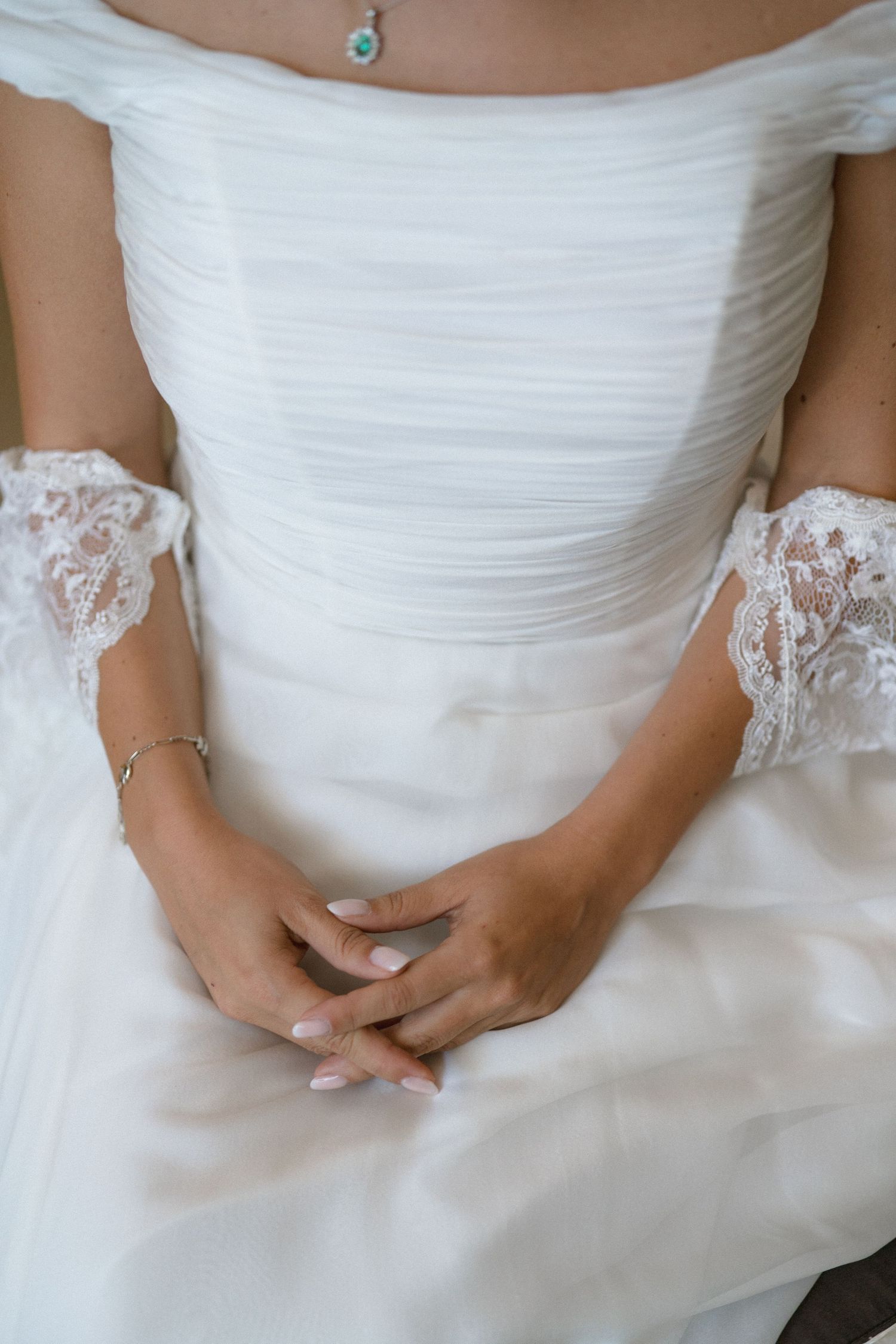 Elegant white wedding dress details showing pleated bodice and delicate lace sleeves.