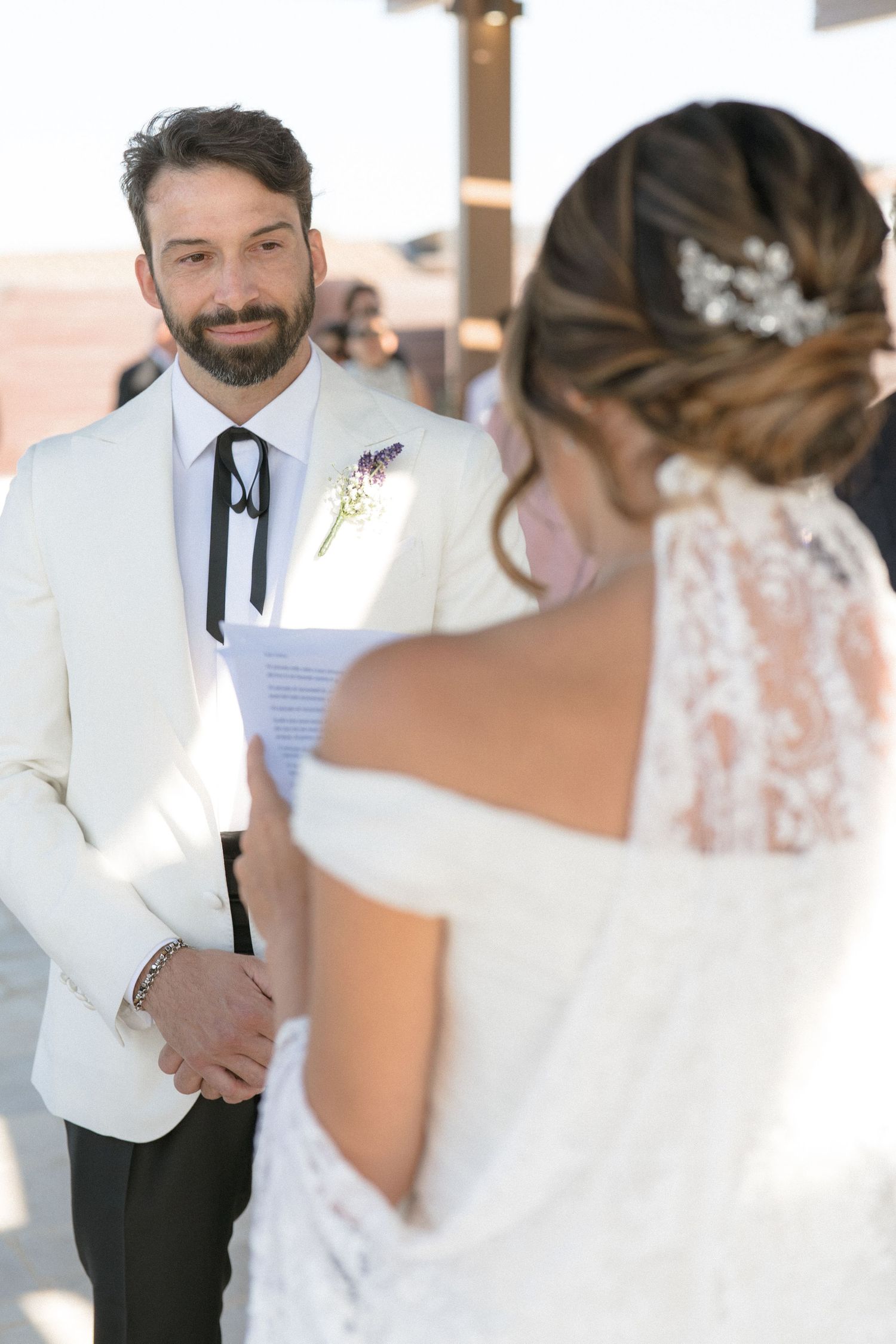 A tender wedding ceremony moment in bright sunlight with elegant white attire and floral details.