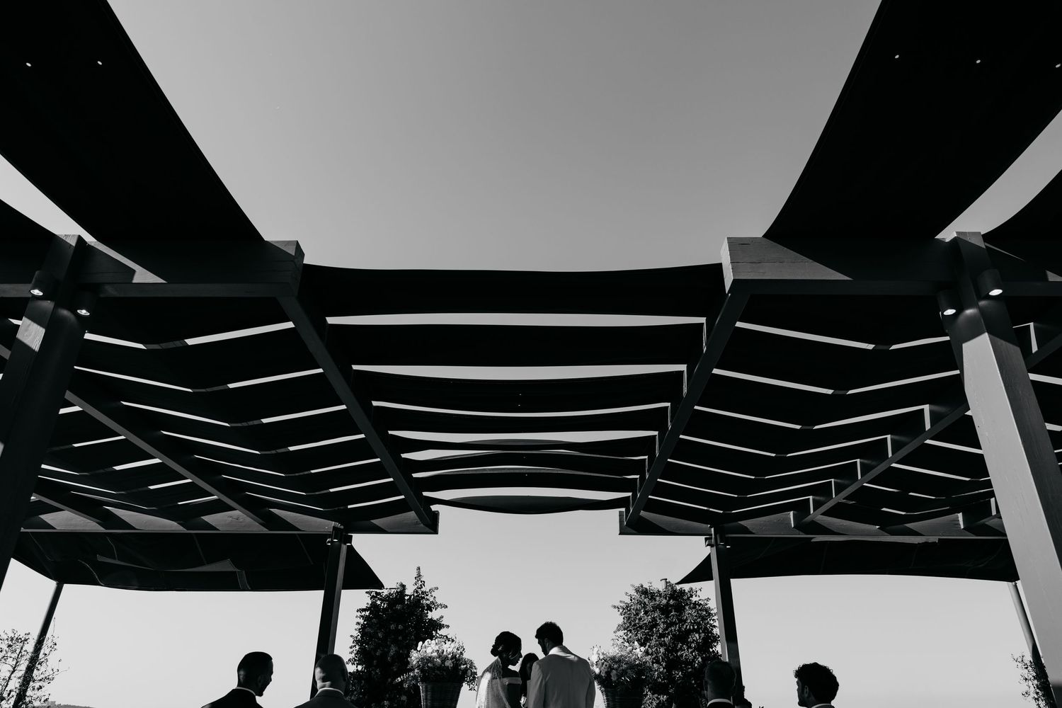 Silhouetted figures under modern geometric shade structure in black and white.