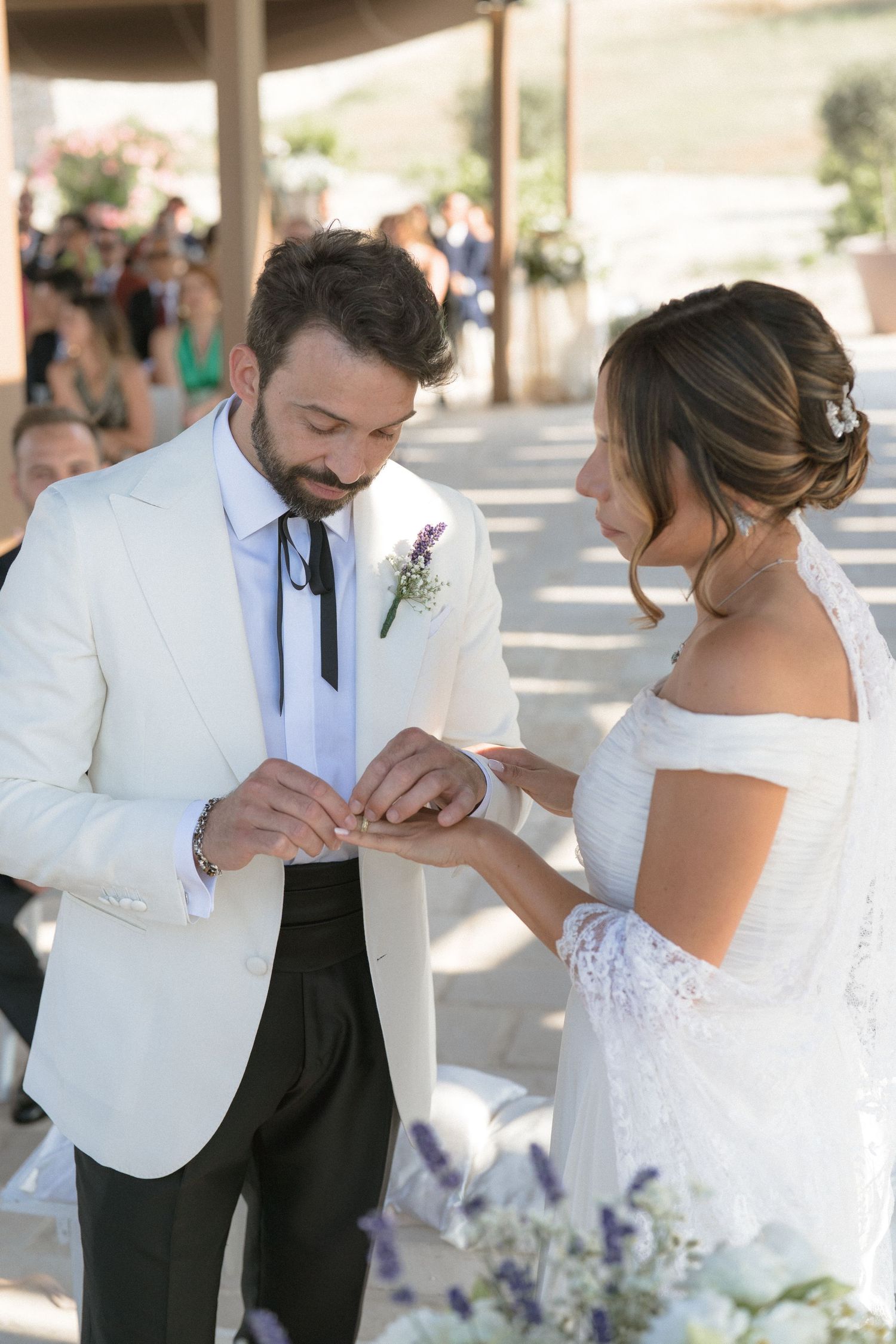 Newlyweds in white attire and formal wear sharing a tender moment during their wedding ceremony.