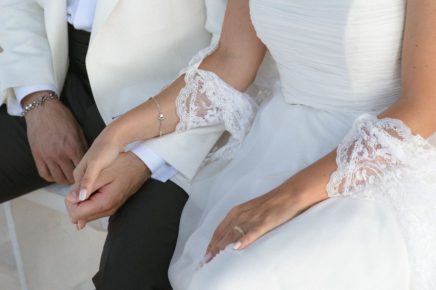 Close-up details of white lace wedding dress and hands during celebration.