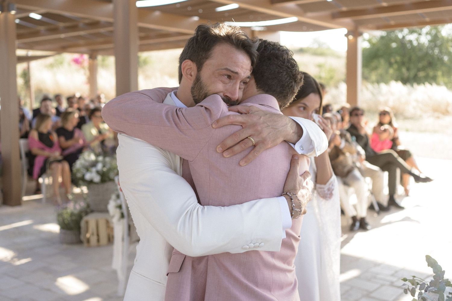An emotional embrace during a wedding ceremony with guests looking on in the background.