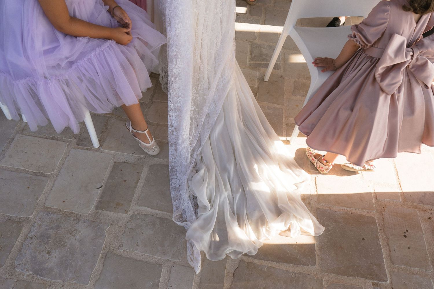 Flowing dress details and shoes photographed in soft natural light on stone flooring.