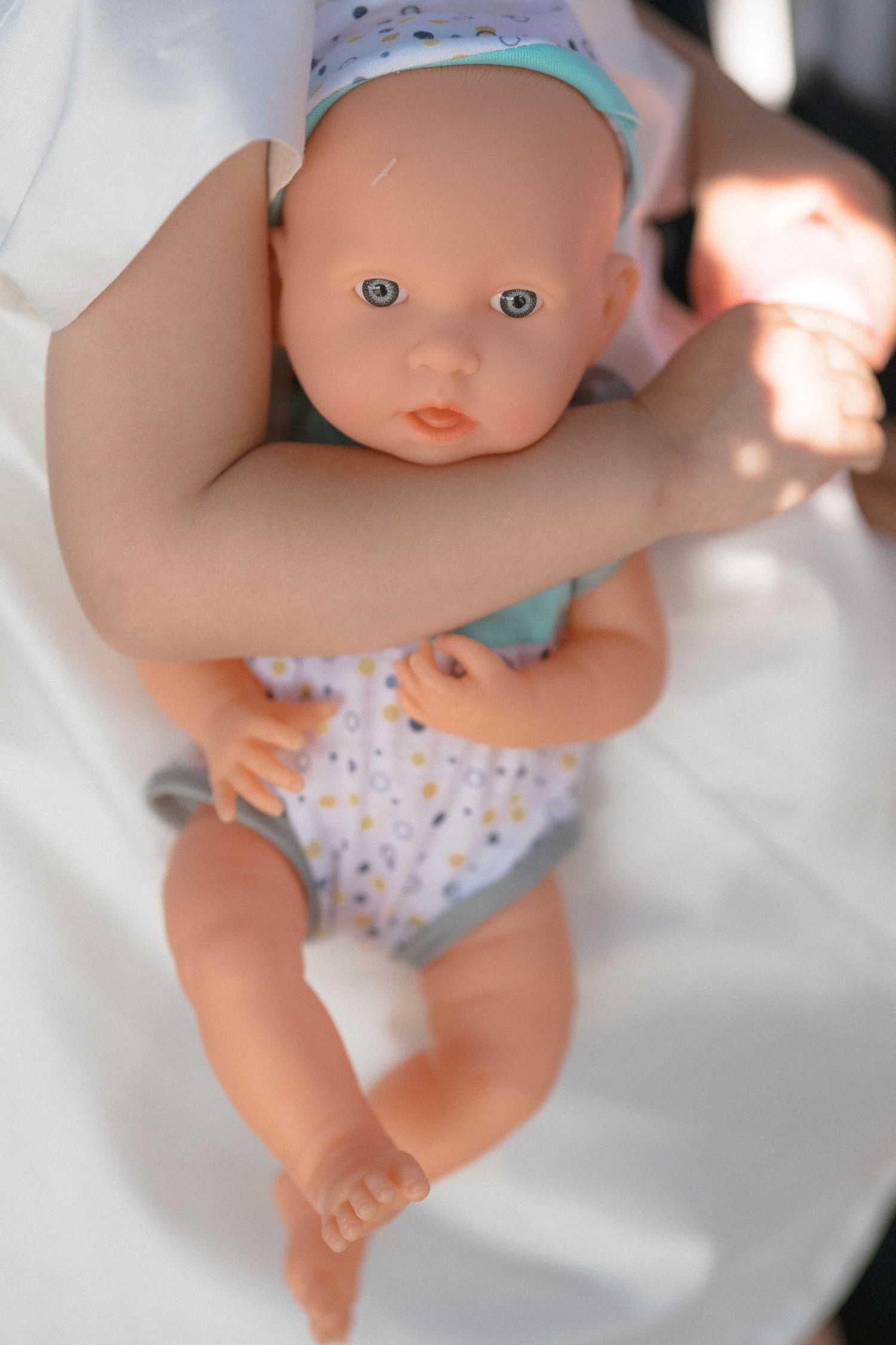 Close-up of a baby doll wearing a floral patterned onesie and mint green headband.