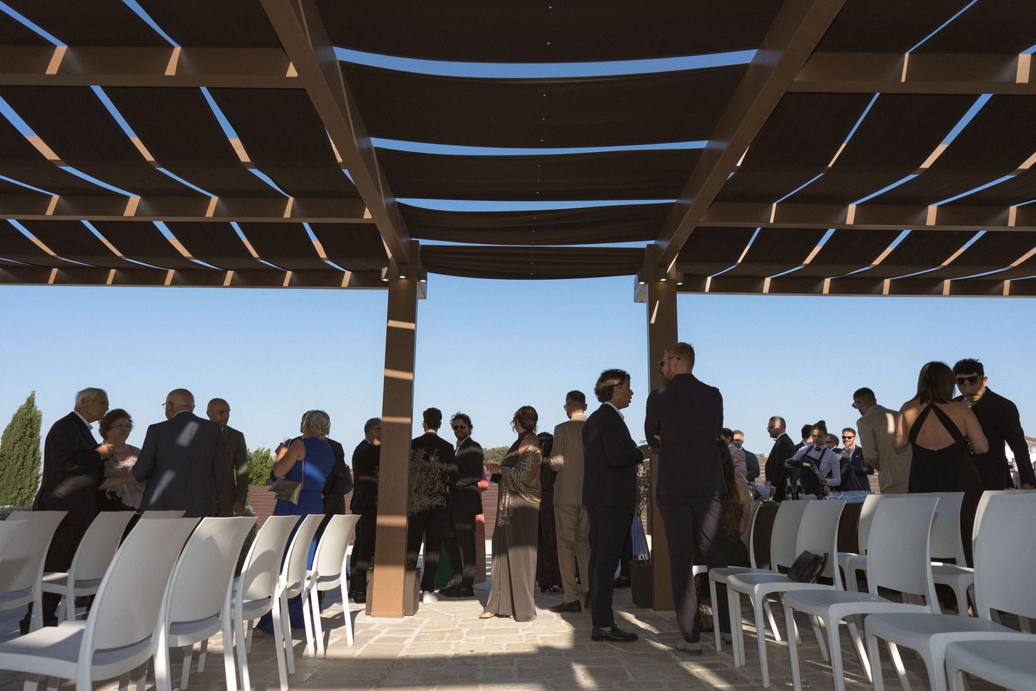 Long wooden pergola with blue sky creates architectural lines and shadows at an outdoor venue.