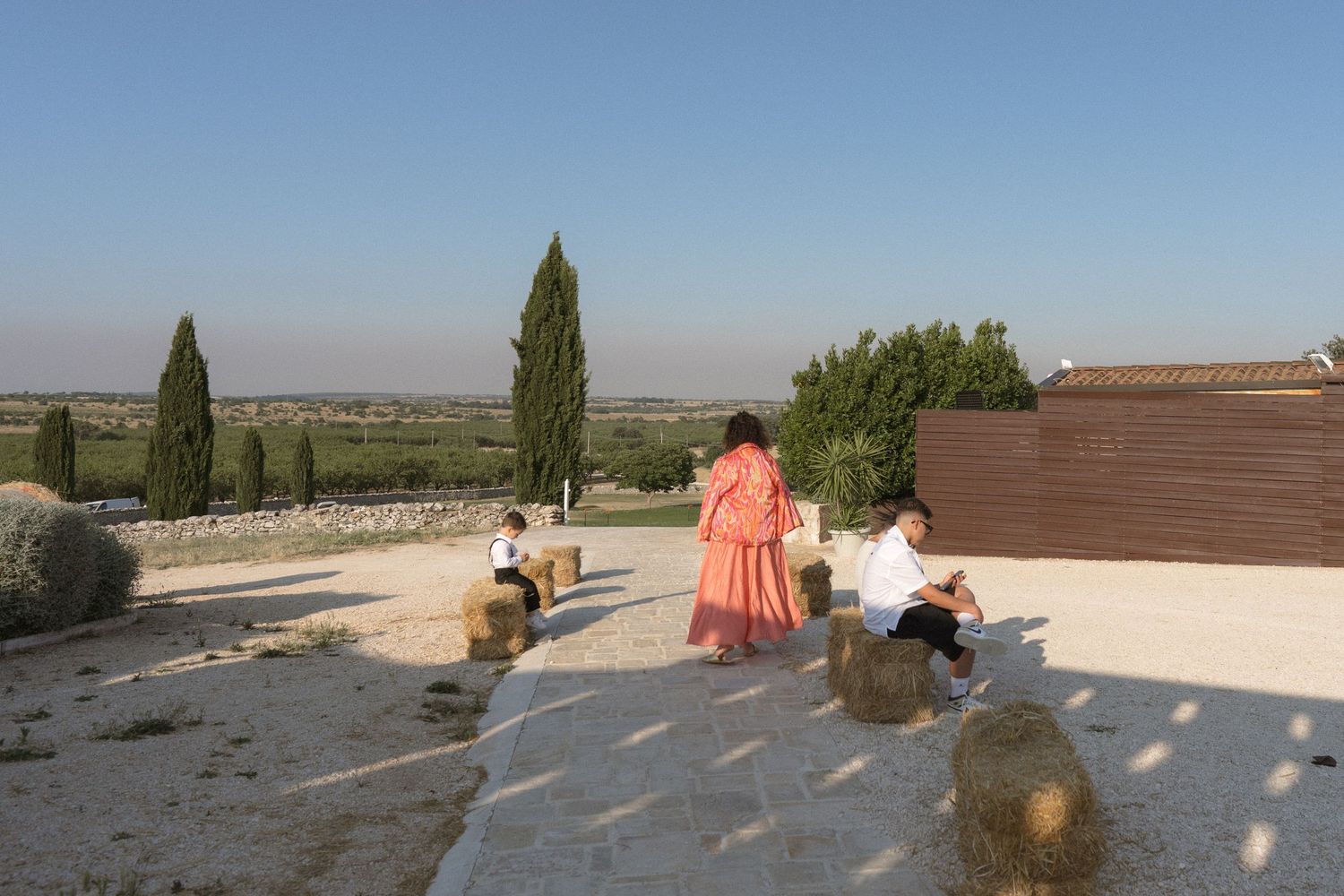 People relaxing on a sunny rooftop terrace with cypress trees and a scenic view of the countryside.