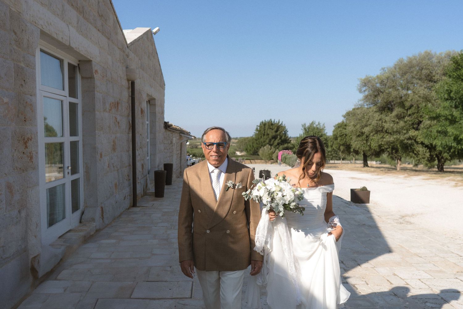 Wedding ceremony taking place outside stone villa under bright summer sky.