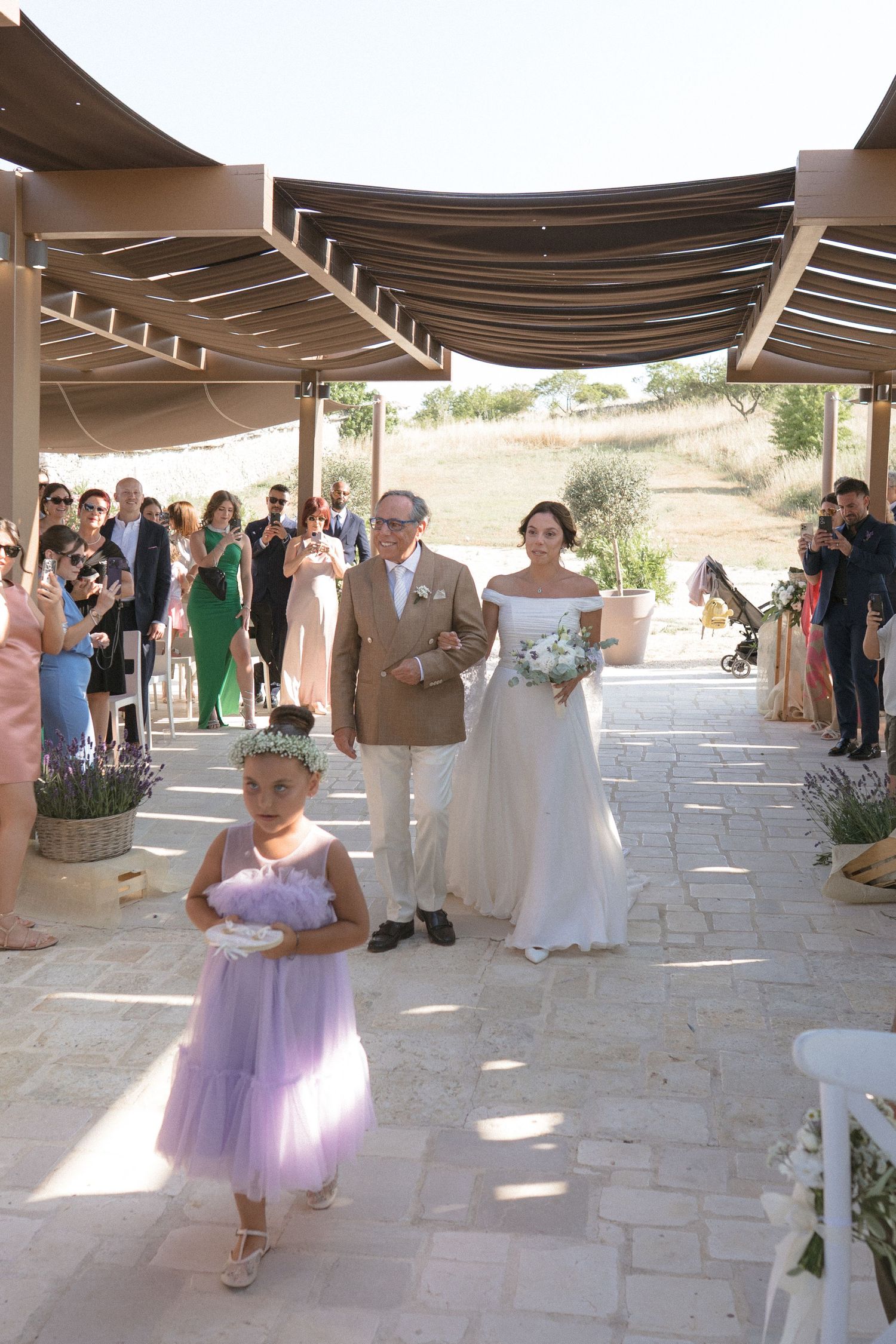 Outdoor wedding ceremony venue with covered patio and flower girl in purple dress walking down the aisle.