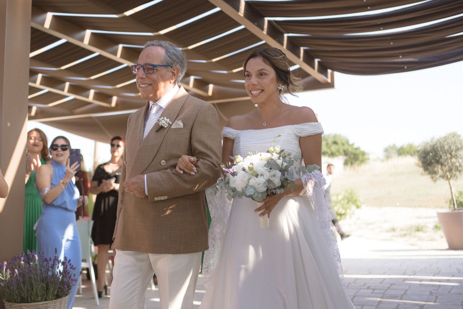 Wedding ceremony setting under wooden pergola with guests gathered to celebrate.