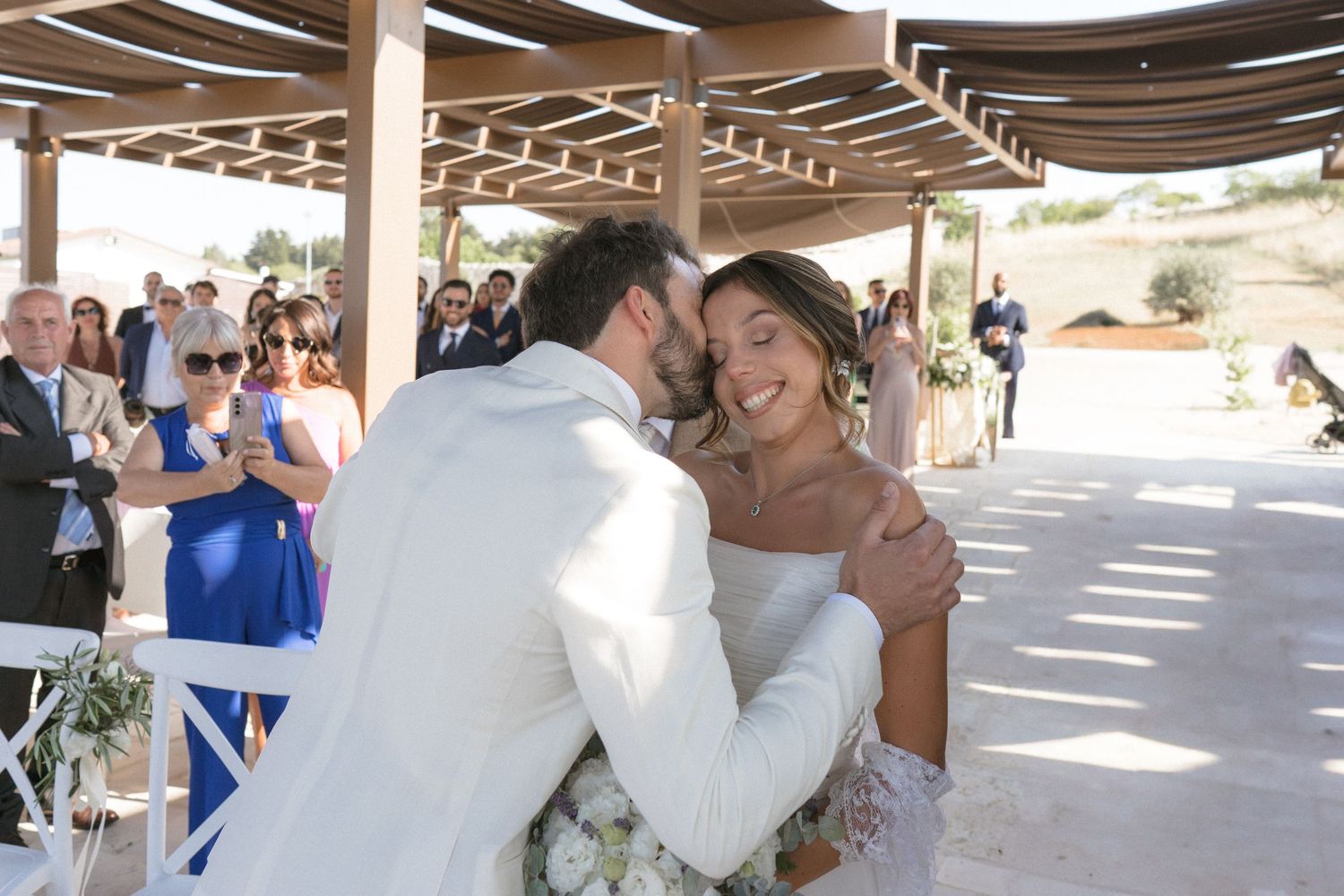 Wedding guests watch and cheer during a first dance at an outdoor reception under a covered patio.