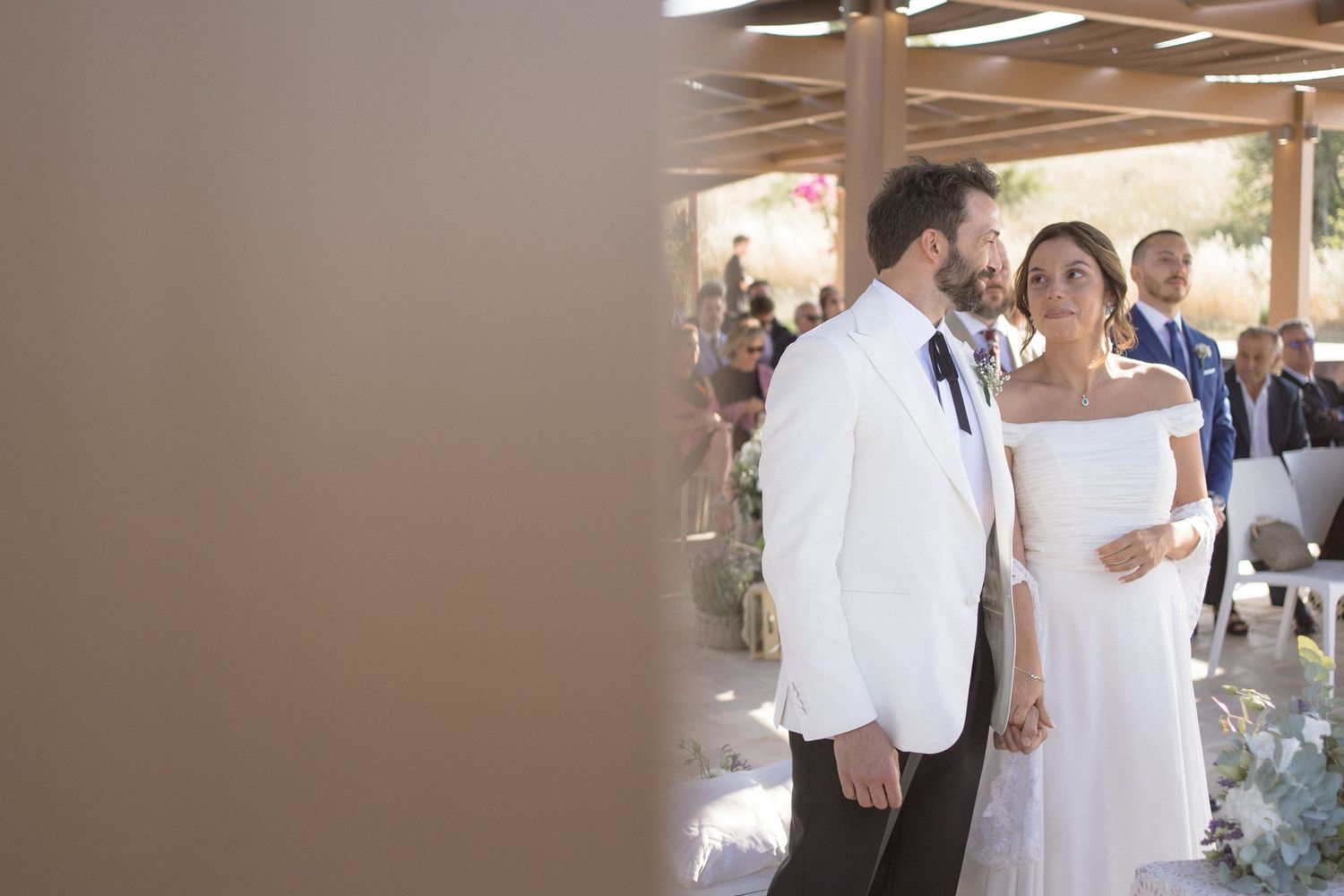 A reception venue decorated in white with people gathering for a wedding celebration.
