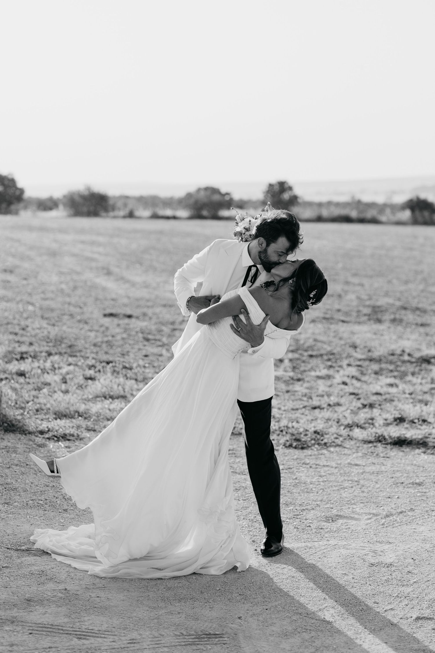 Romantic black and white photo of couple dancing and dipping in an outdoor field.