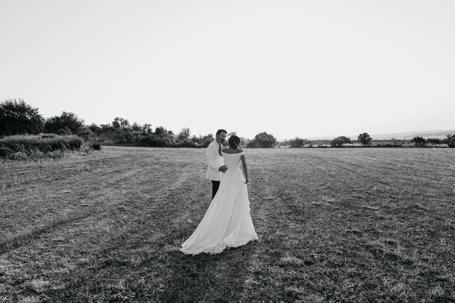 A black and white photograph of a couple walking through a vast open field.