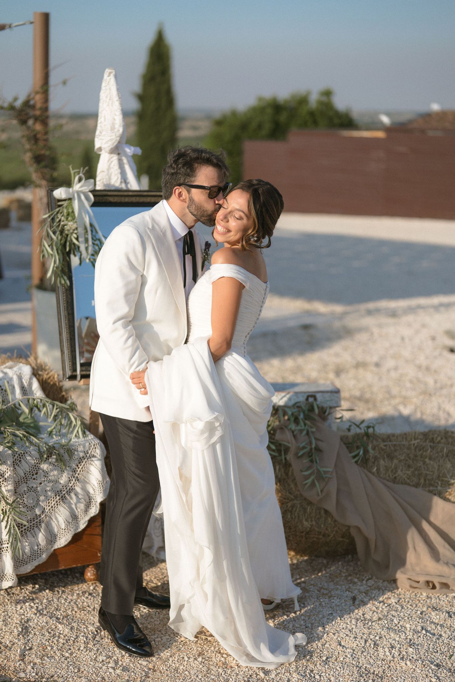 A romantic couple in wedding attire sharing intimate moments on a stone-paved beach setting at sunset.