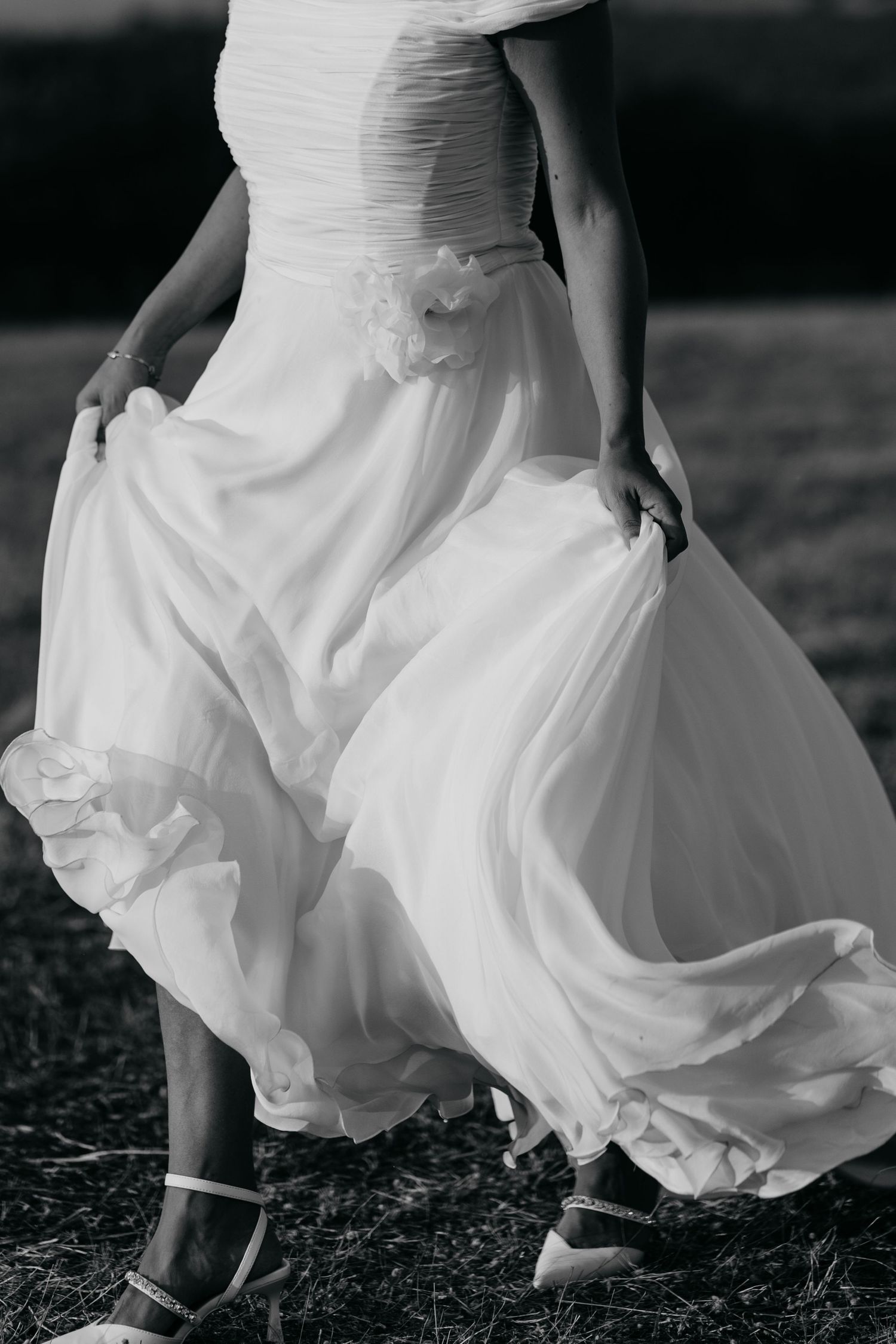 Close up of flowing white wedding dress and strappy heels showing movement and texture in black and white.