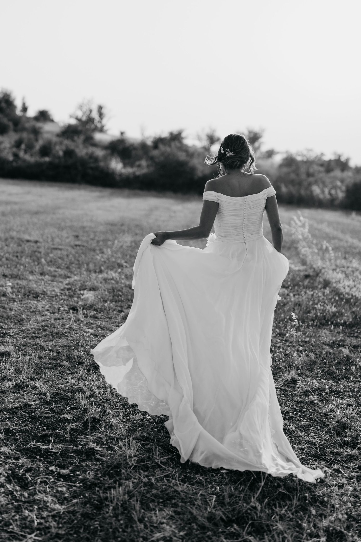 Flowing white dress flows dramatically in the wind against a rural hillside setting.