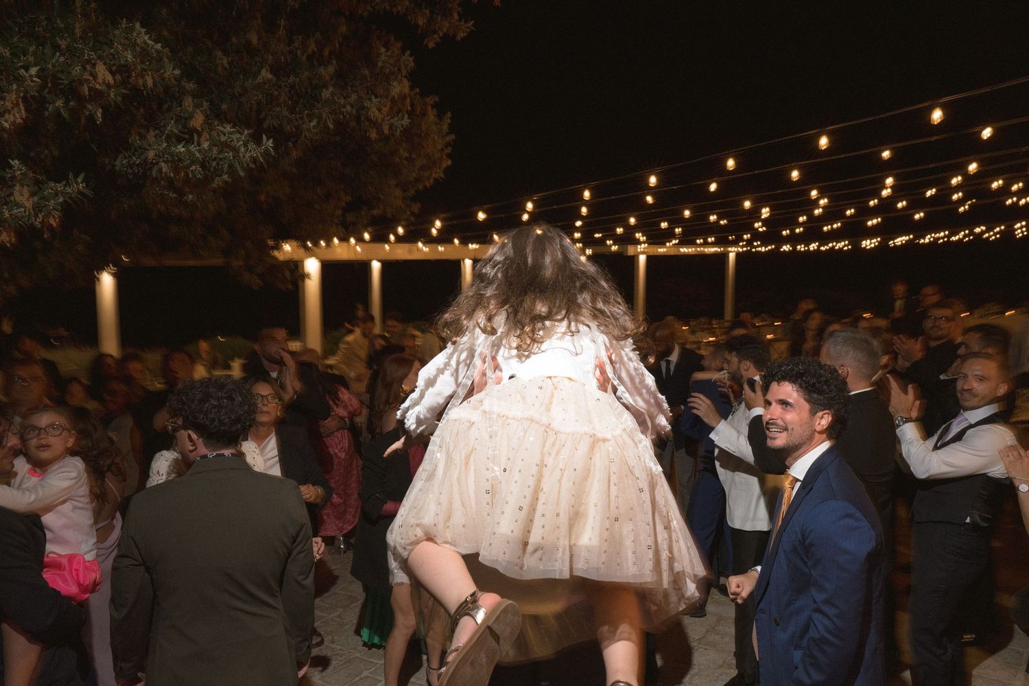 Guests celebrating at an outdoor reception under string lights with a dance floor.