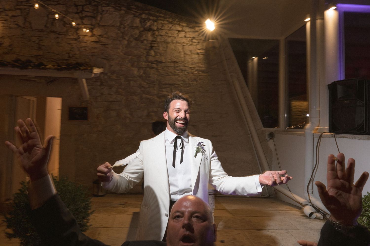 Partygoers dancing and celebrating at a lively wedding reception with string lights and exposed brick walls.
